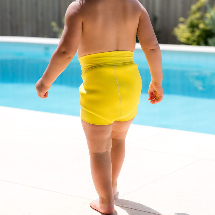 Close up of little one wearing neoprene swim diaper in bright yellow, front.