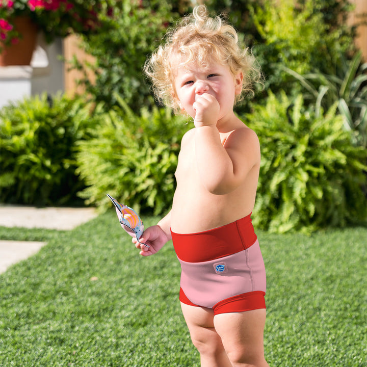 Little one wearing neoprene swim diaper in pink with red ribs.