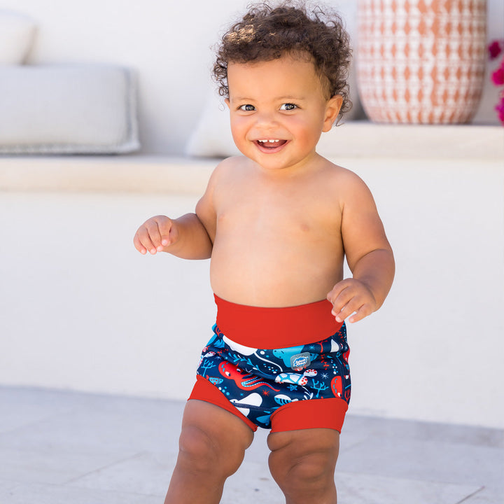 Little one wearing neoprene swim diaper in blue with red ribs, featuring under the sea themed print.