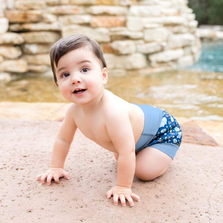 Little one wearing neoprene swim diaper in blue, featuring sharks themed print. 