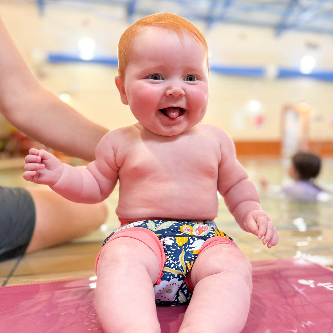 Little one wearing neoprene swim diaper in navy with pink trims, and floral themed print.