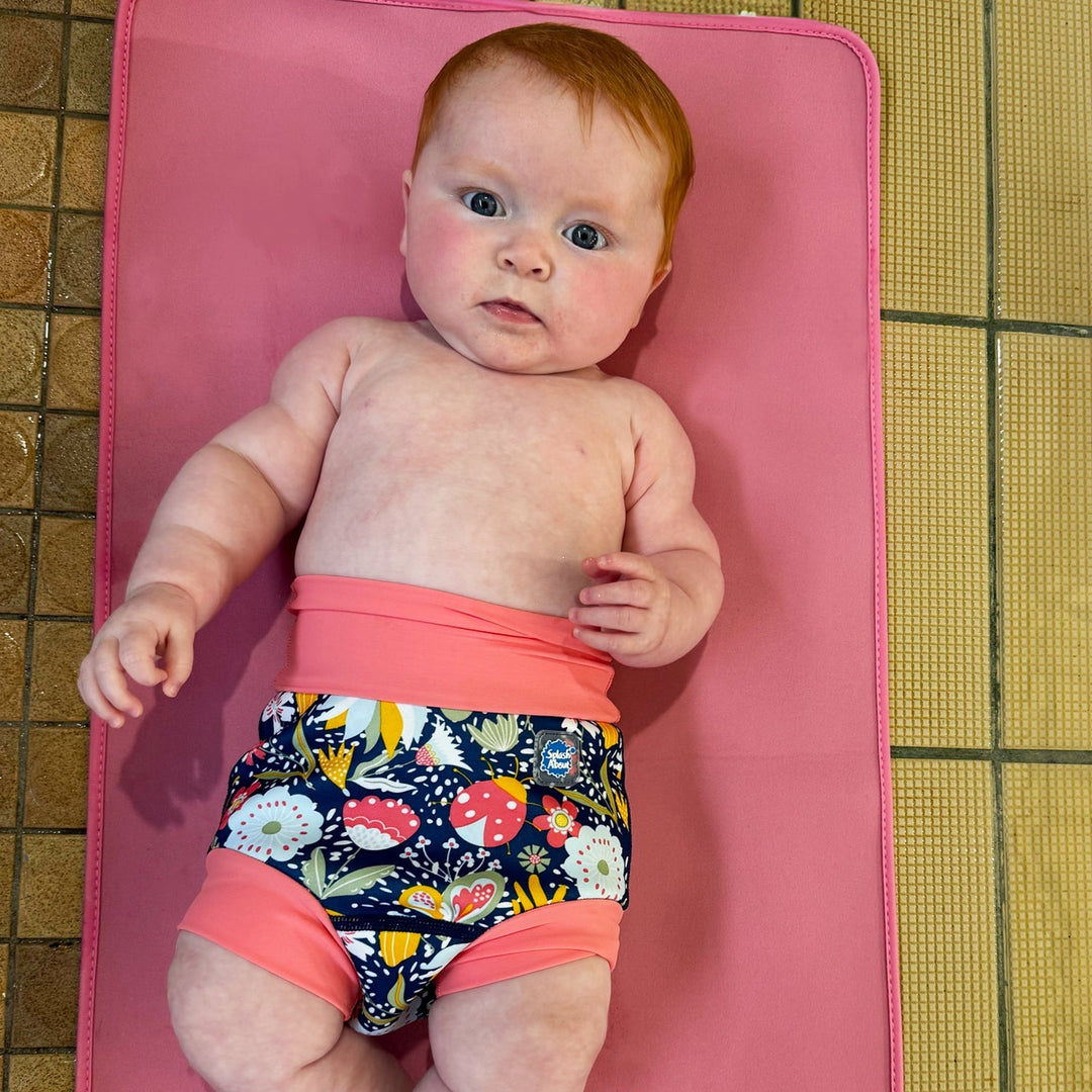 Little one wearing neoprene swim diaper in navy with pink trims, and floral themed print.