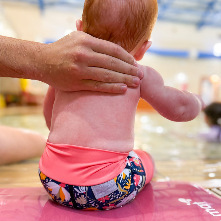 Little one wearing neoprene swim diaper in navy with pink trims, and floral themed print.