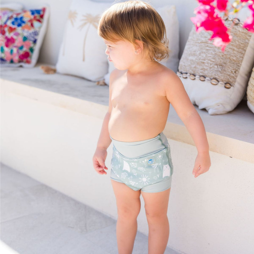 Little one wearing Happy Nappy in greenish blue, featuring animals themed print in white. Side.