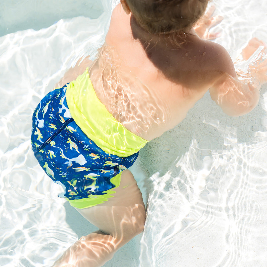 Little one wearing neoprene swim diaper in navy, with lime ribs and turtles themed print.