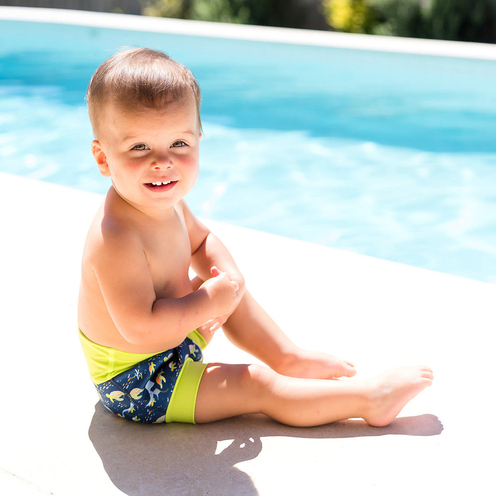 Little one wearing neoprene swim diaper in navy, with lime ribs and turtles themed print.