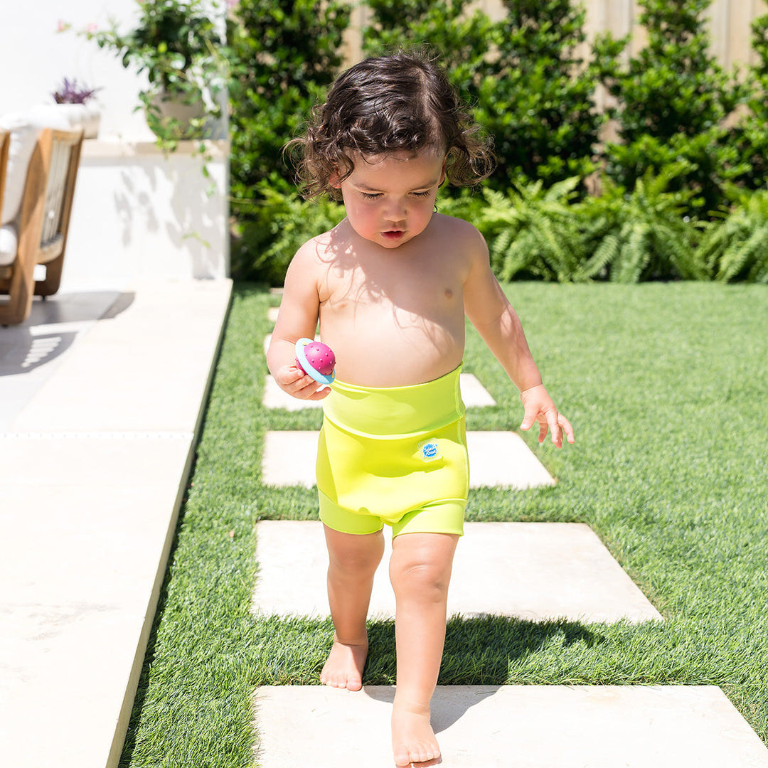 Little one wearing neoprene swim diaper in bright lime green, poolside.