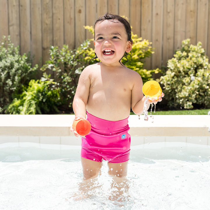 Little one wearing neoprene swim diaper in hot pink, playing in the pool.