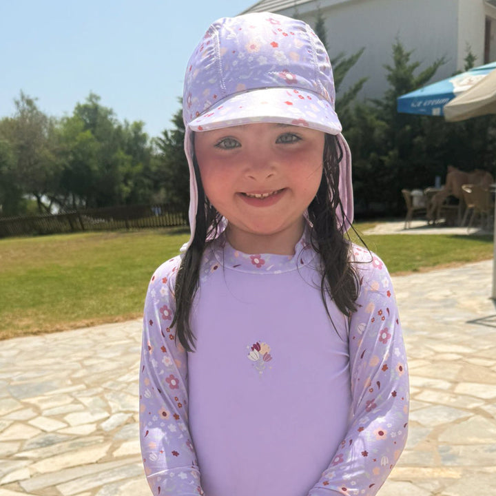 Little one wearing legionnaire style sun hat in lilac, with floral themed print panel. She is also wearing matching rash gard.