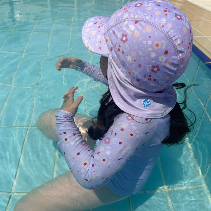 Little one wearing legionnaire style sun hat in lilac, with floral themed print panel. She is also wearing matching rash gard.