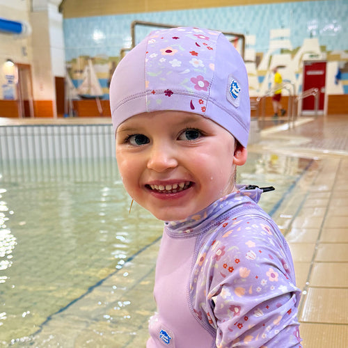 Little one wearing baby swim hat in lilac featuring floral themed print.