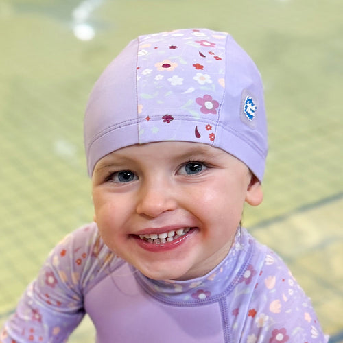 Little one wearing baby swim hat in lilac featuring floral themed print.