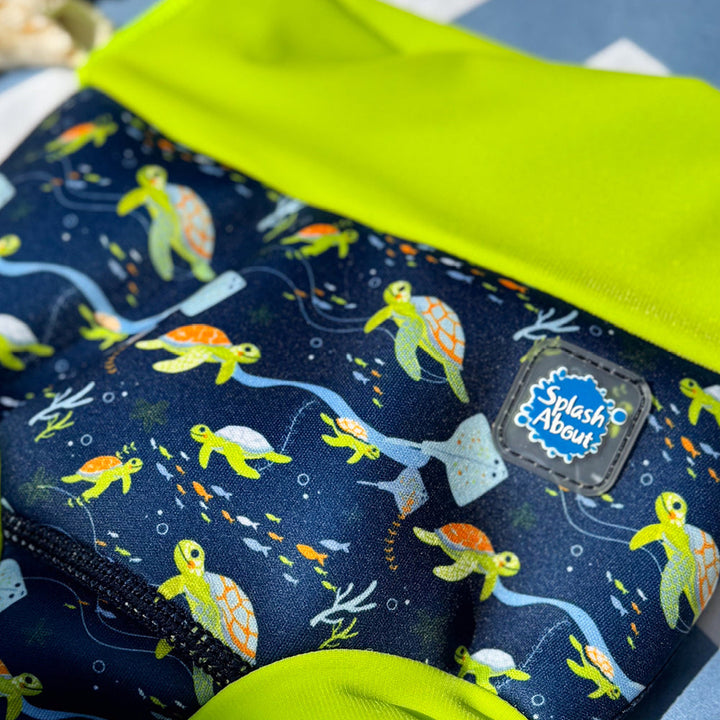 Little one wearing neoprene swim diaper in navy, with lime ribs and turtles themed print.