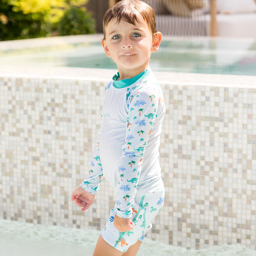 Child wearing neoprene swim shorts in mint and dinosaurs themed print. He's also wearing matching rash top.
