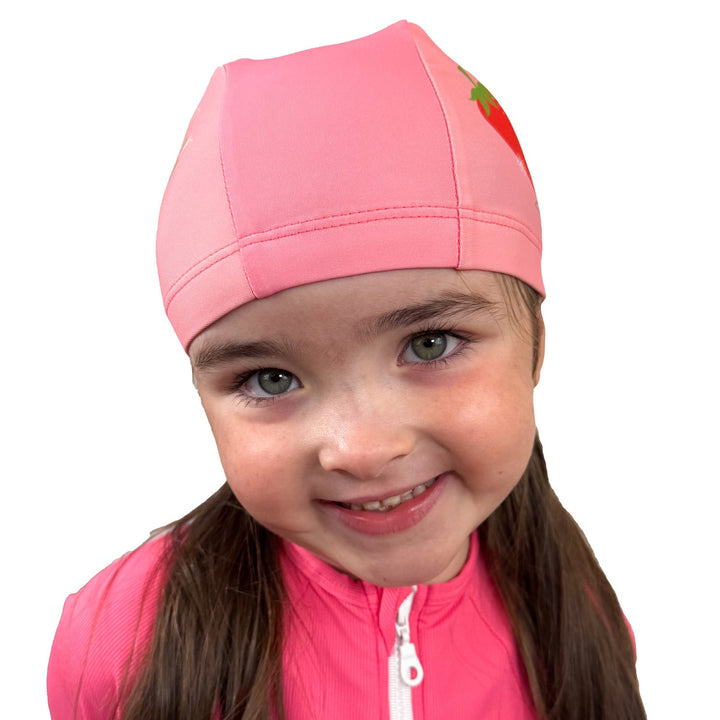 Little one wearing baby swim hat in pink featuring strawberries themed print.