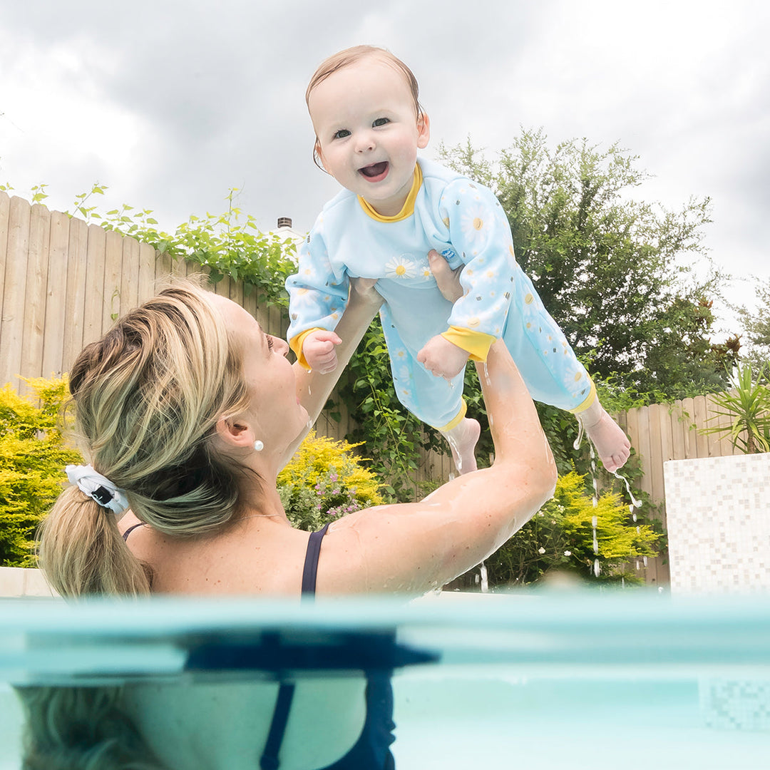 Little one wearing fleece-lined baby wetsuit in baby blue with yellow trims and daisies themed print.