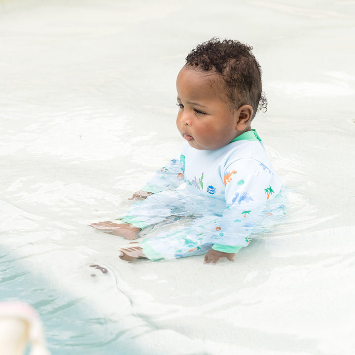Little one wearing fleece-lined baby wetsuit in baby blue with mint trims and dinosaurs themed print.