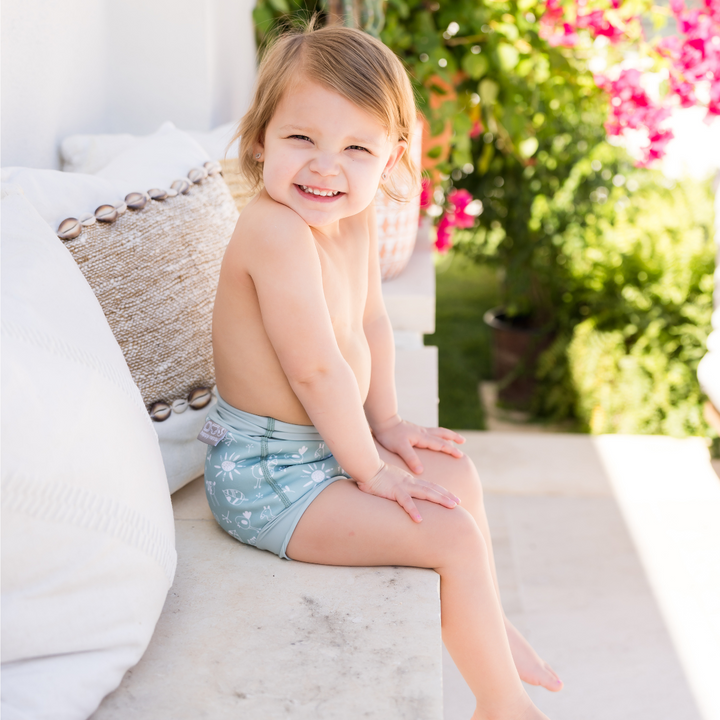 Lifestyle image of little one wearing swim nappy, sitting down.